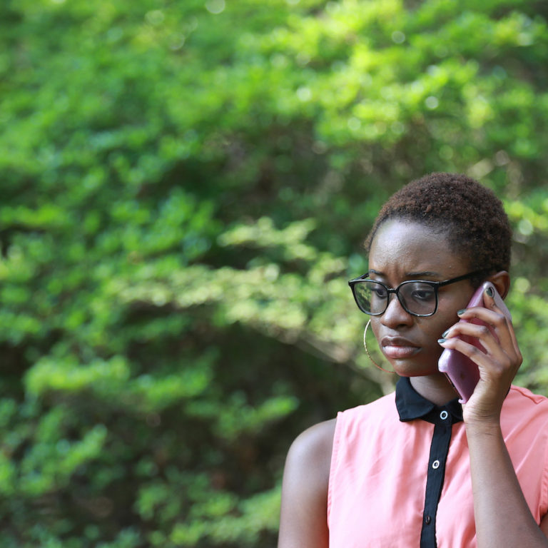Young contemporary African woman looking gloomy and upset while speaking on phone in park